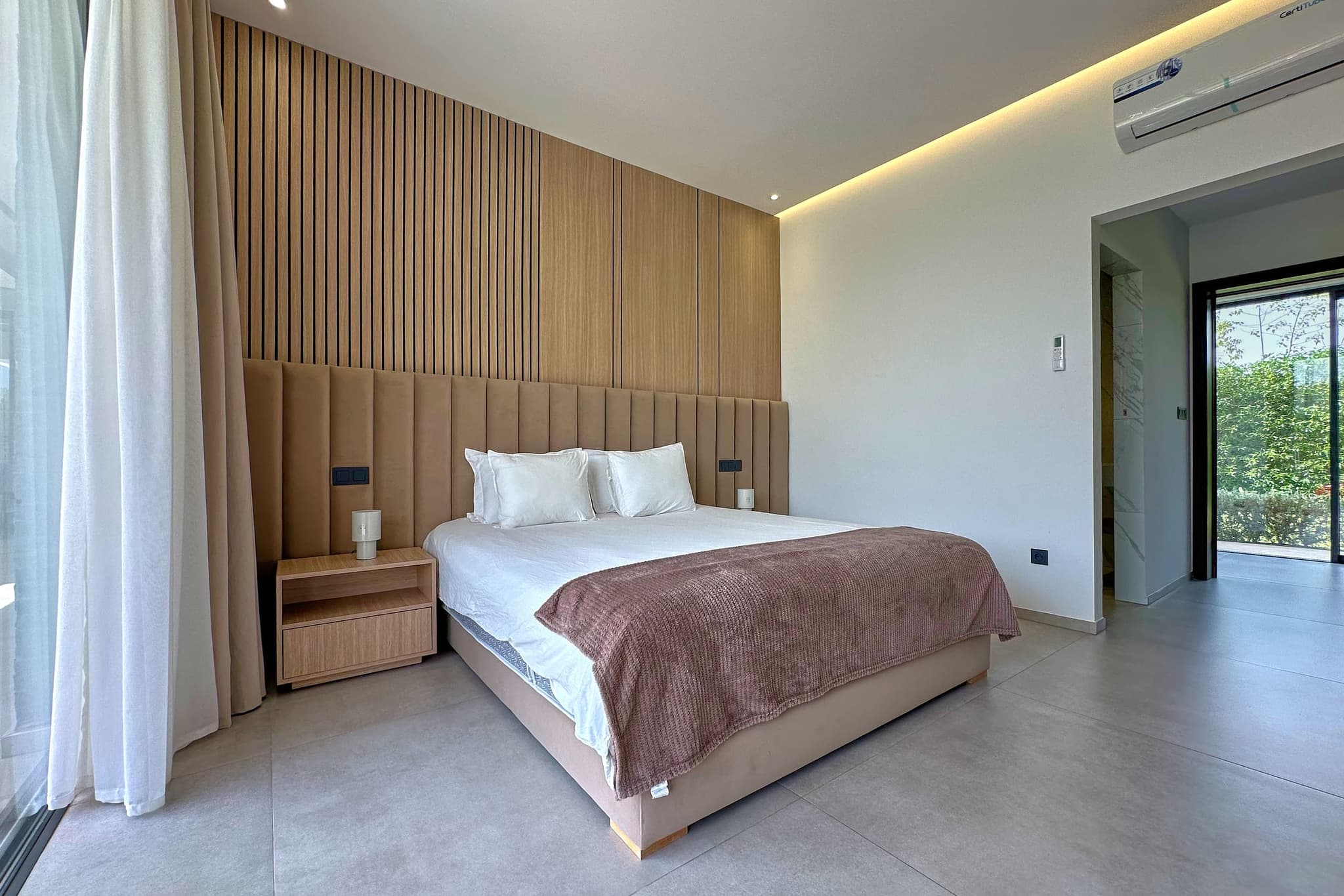 Une des trois chambres : lit double devant une tête de lit capitonnée, mur de lattes verticales.