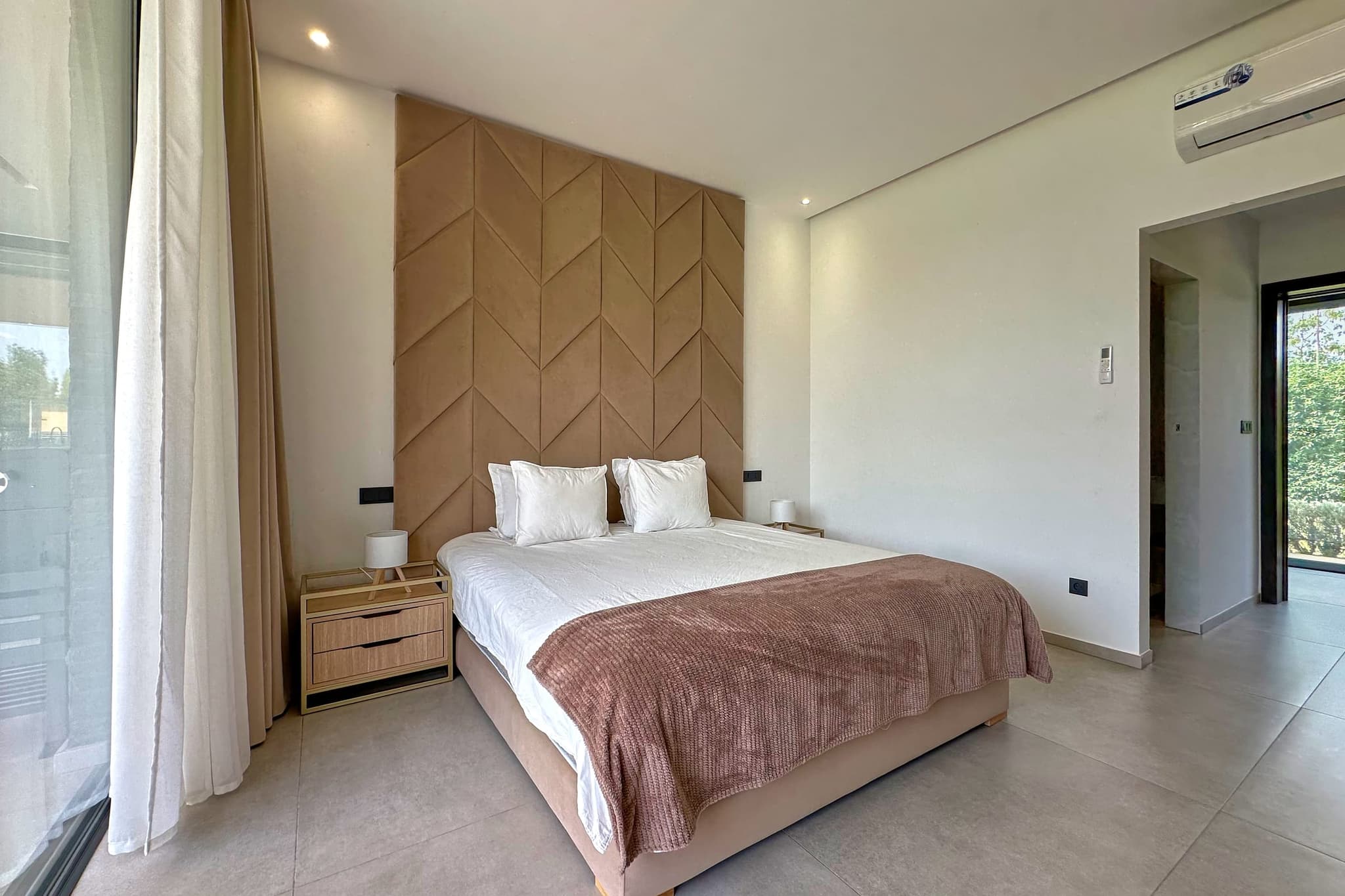 Une des trois chambres : lit double, tête de lit capitonnée à chevrons, porte sur le jardin.