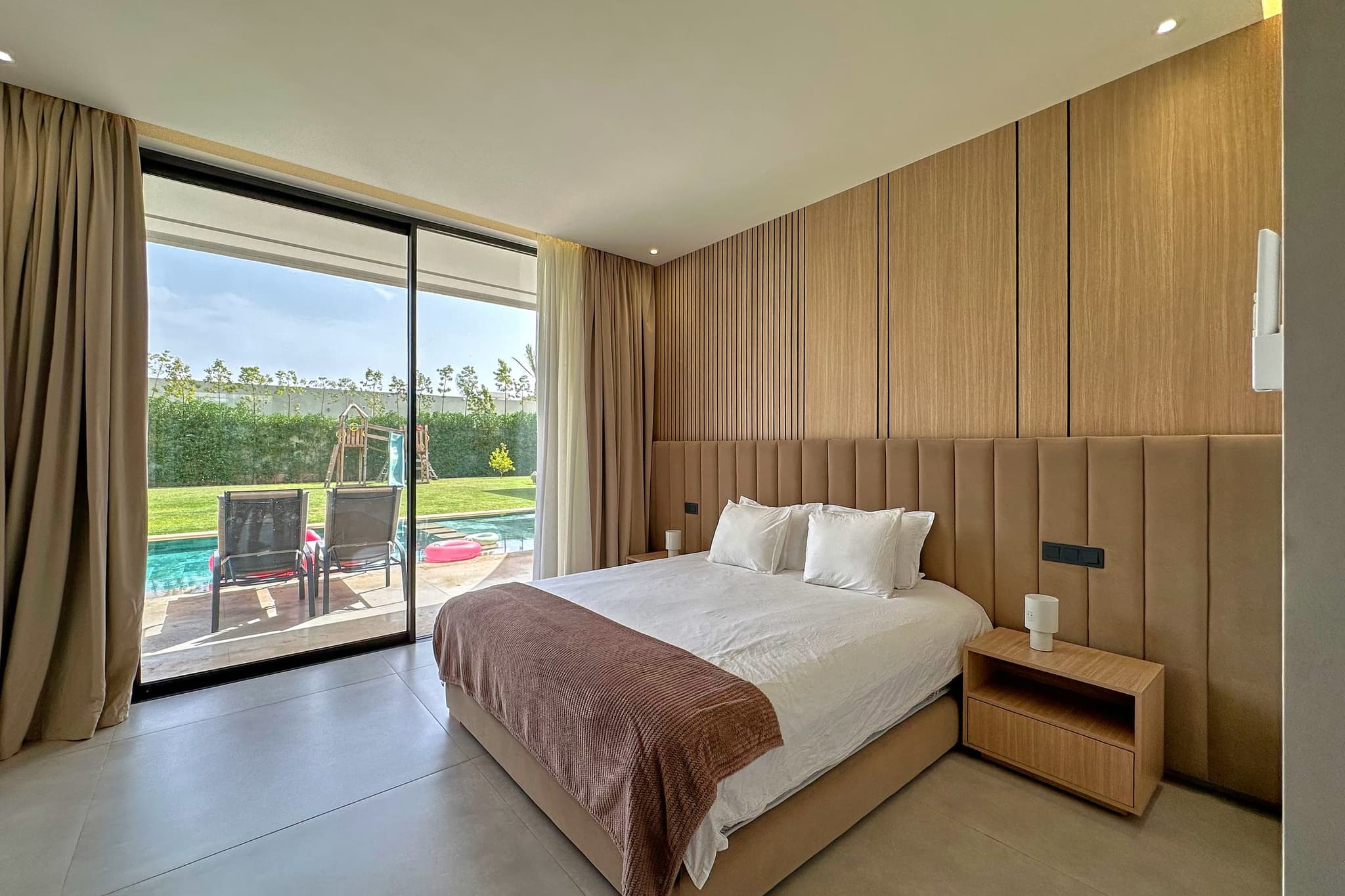 La même chambre vue vers la baie vitrée, qui donne sur la pelouse et la piscine.