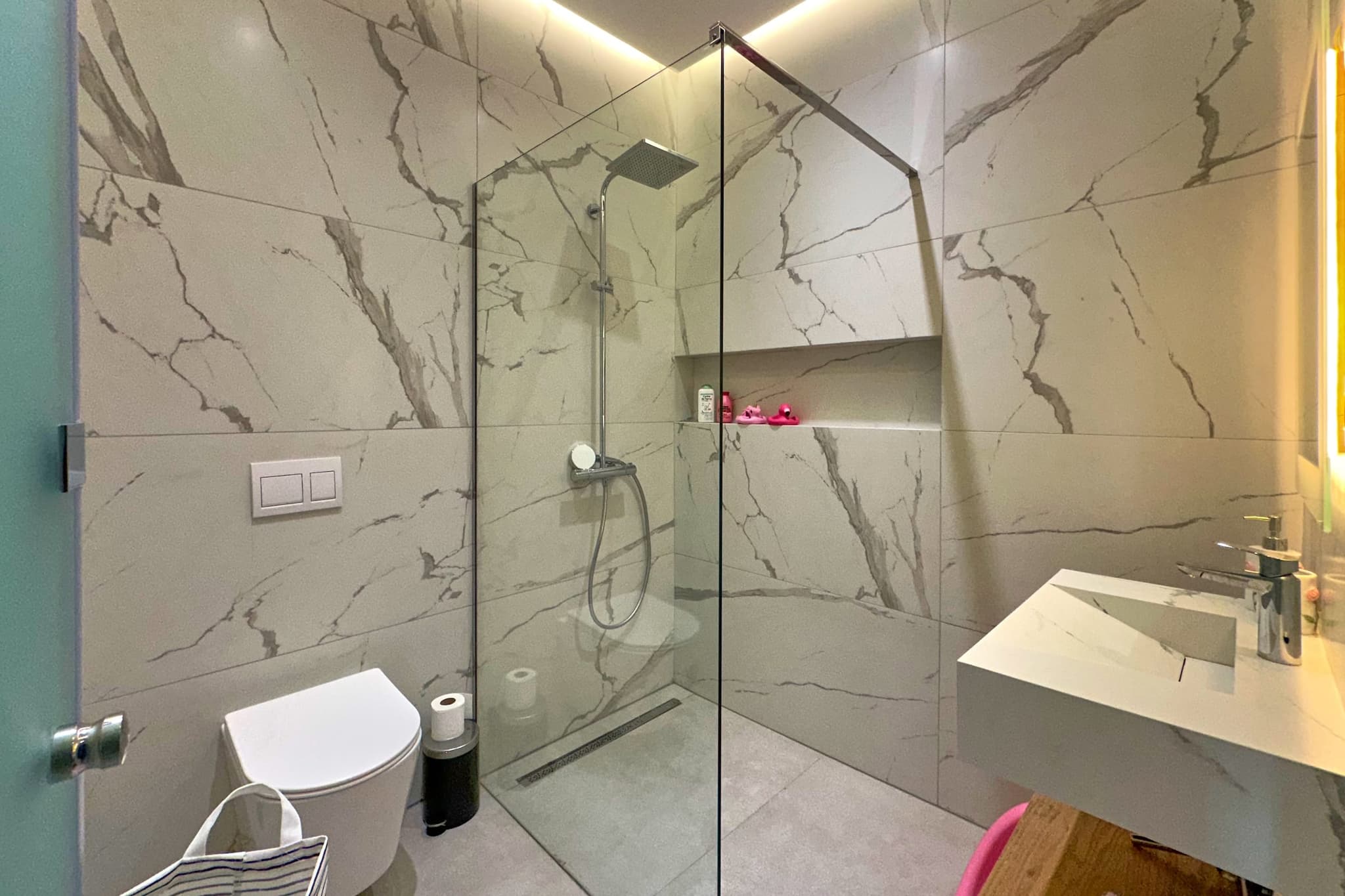 Salle de bain : douche à l’italienne fermée par une paroi de verre, marbre blanc du sol au plafond.