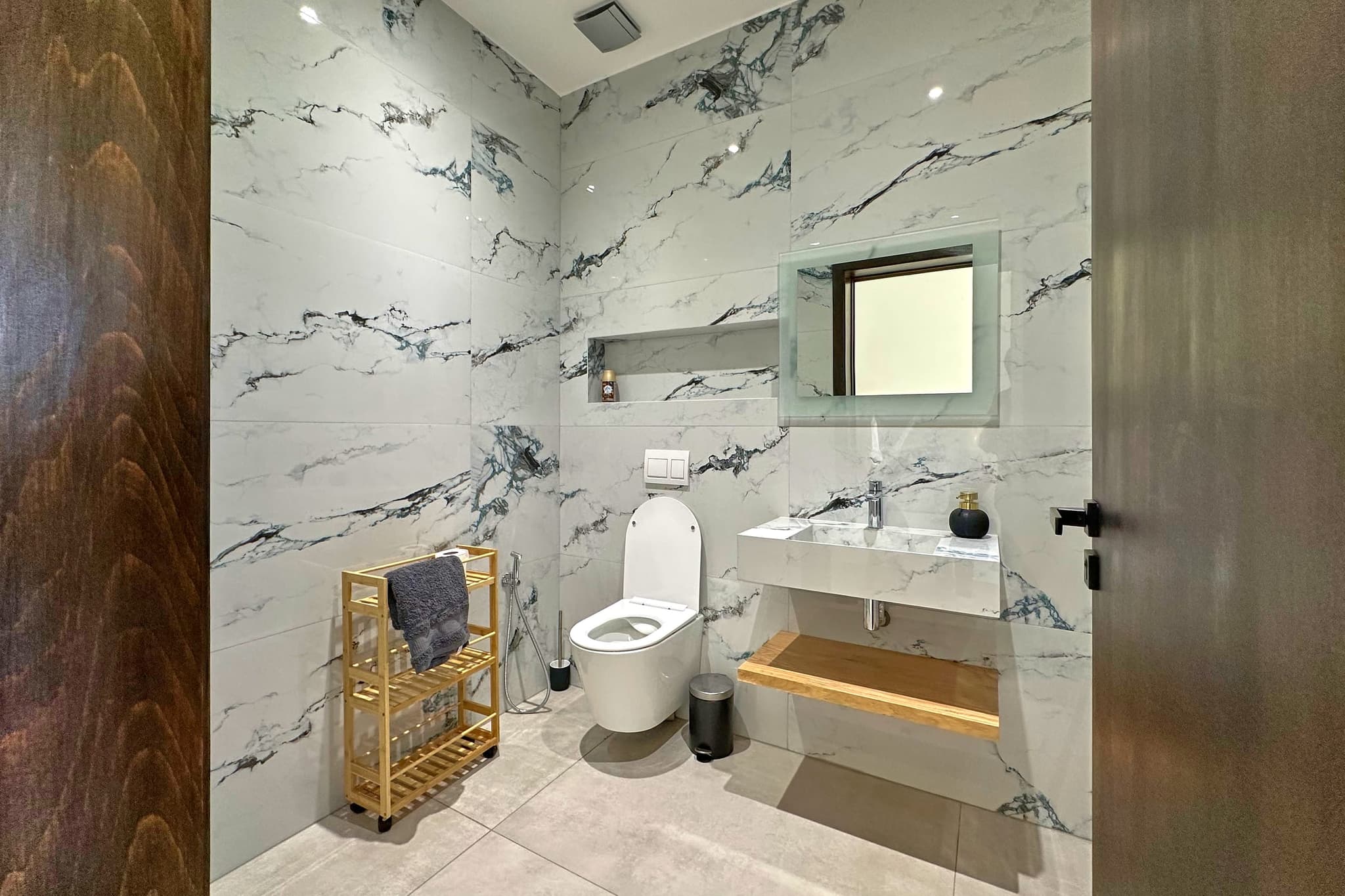 Salle de bain en marbre blanc veiné : vasque suspendue, miroir, porte-serviettes en bois.