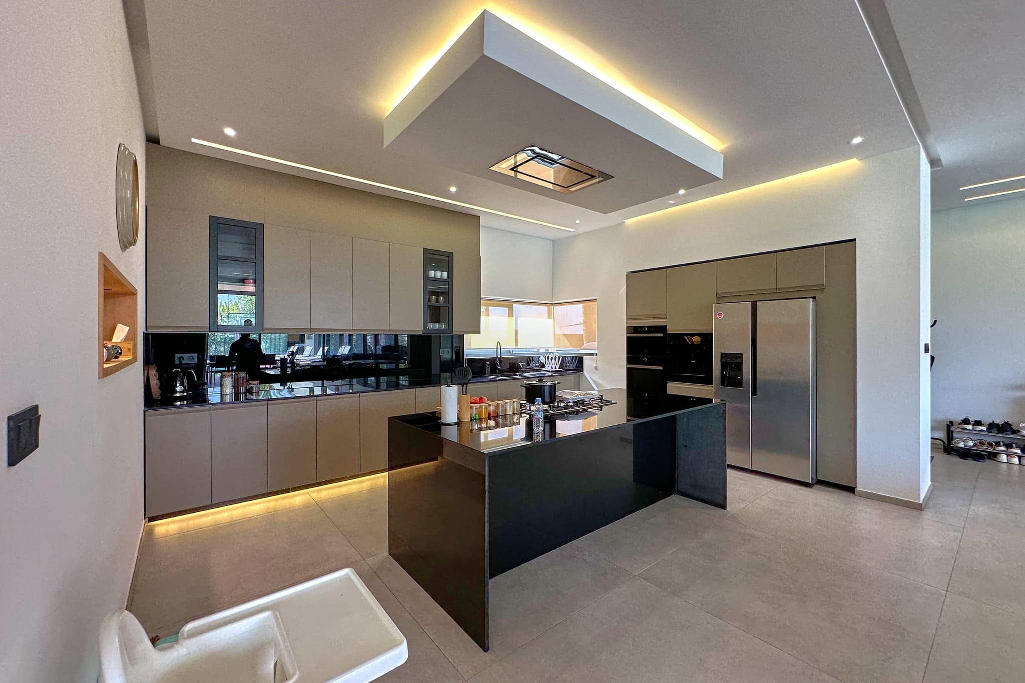 La cuisine : îlot central noir, façades claires, fours encastrés et réfrigérateur américain.