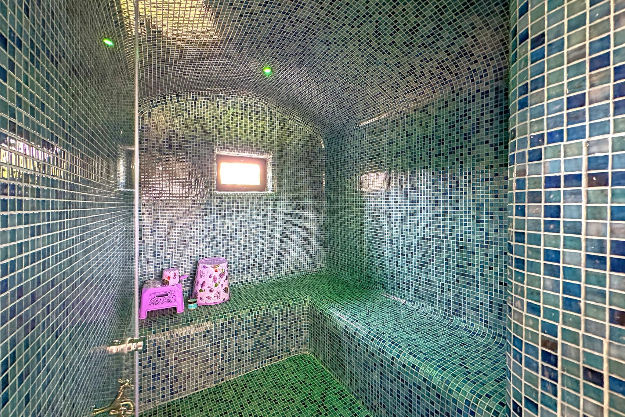 Le hammam, voûte et banquette entièrement couvertes de mosaïque verte et bleue.