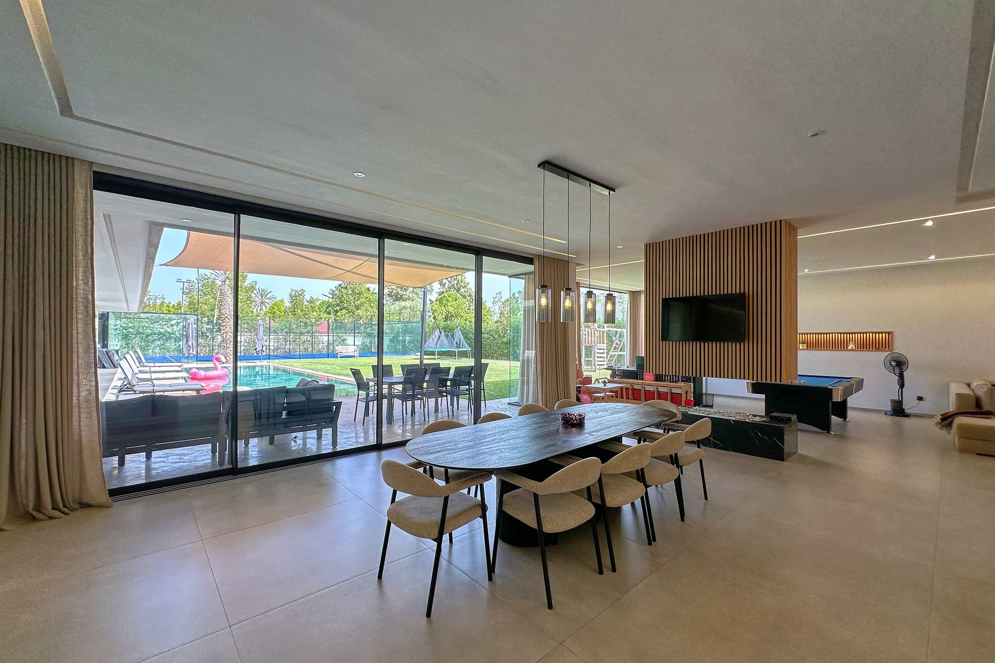 La grande table à manger et ses chaises, devant une baie vitrée ouverte sur la piscine.