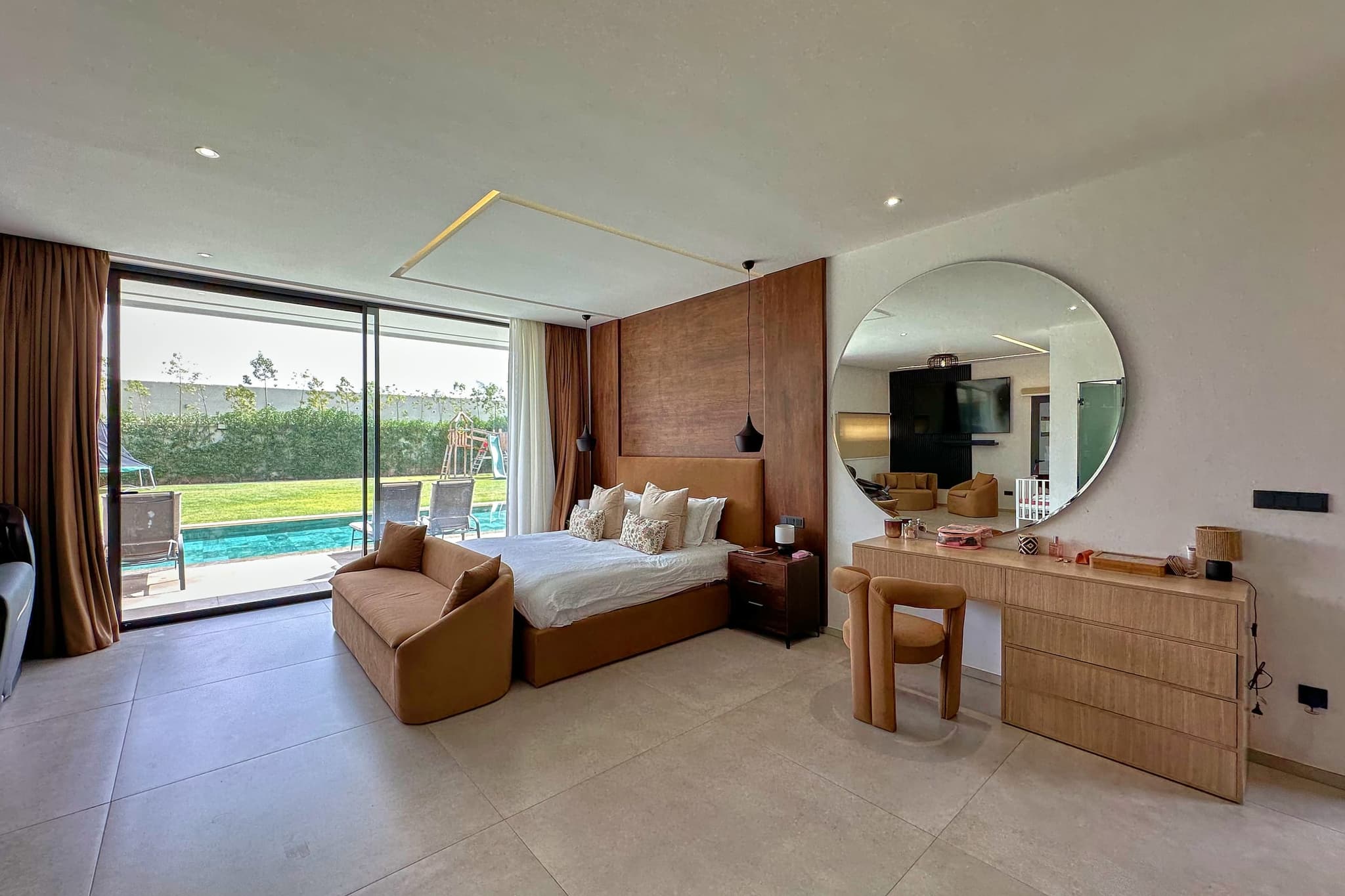 La suite : lit double devant un mur de bois, grand miroir rond, coiffeuse, baie vitrée sur la piscine.